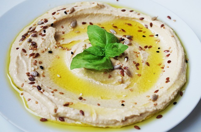 Assiette contenant de la purée de pois chiche arrosée d'huile d'olive, de graines de sésame et avec des feuilles de basilic