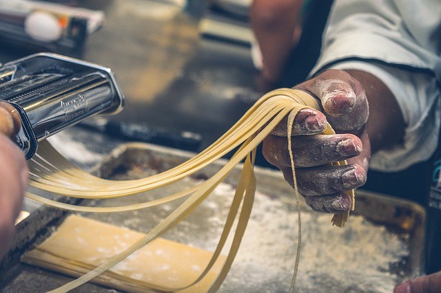 Main avec de la farine qui tient des pâtes fraîche sortant d'un laminoire