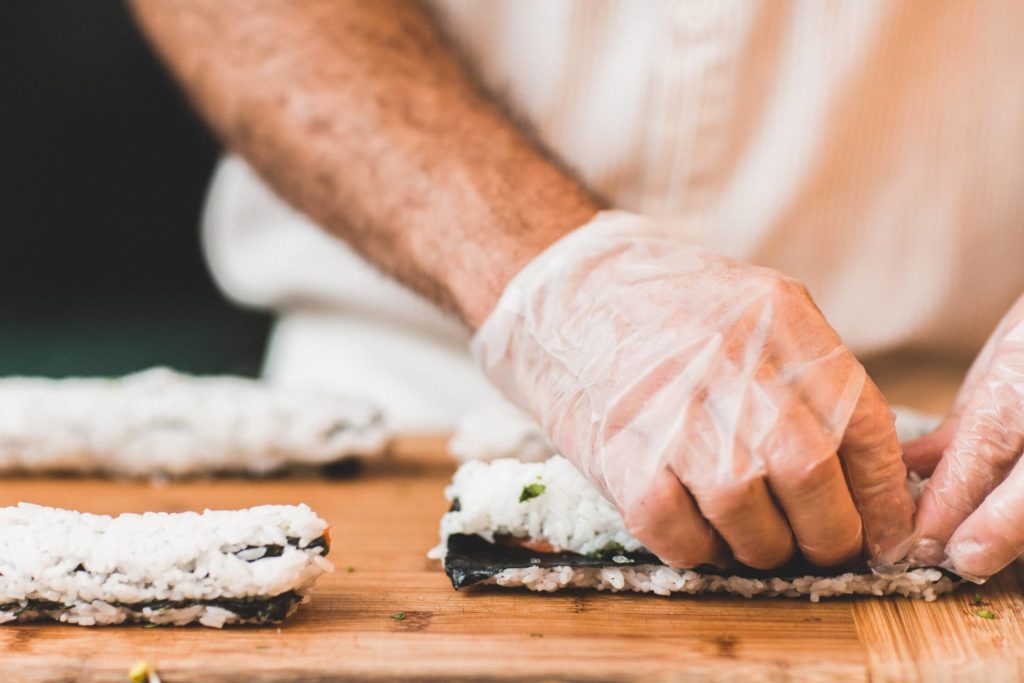 Main gantée qui réalise des sushis