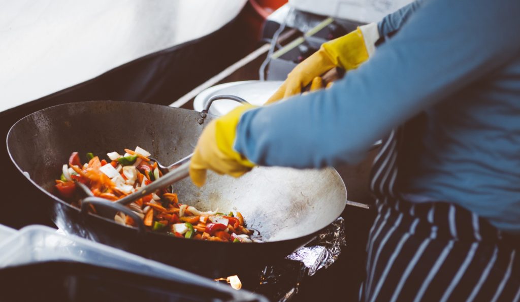 Main tenant une louche qui cuisine des légumes au wok