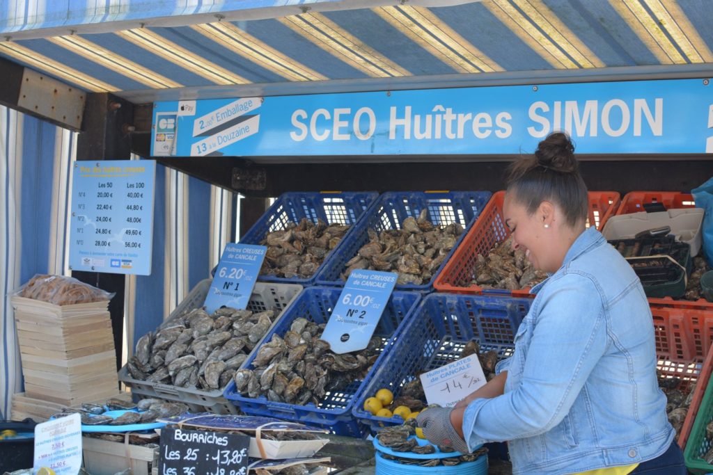 Femme souriante à son stand d'huîtres au marché qui ouvre une huître