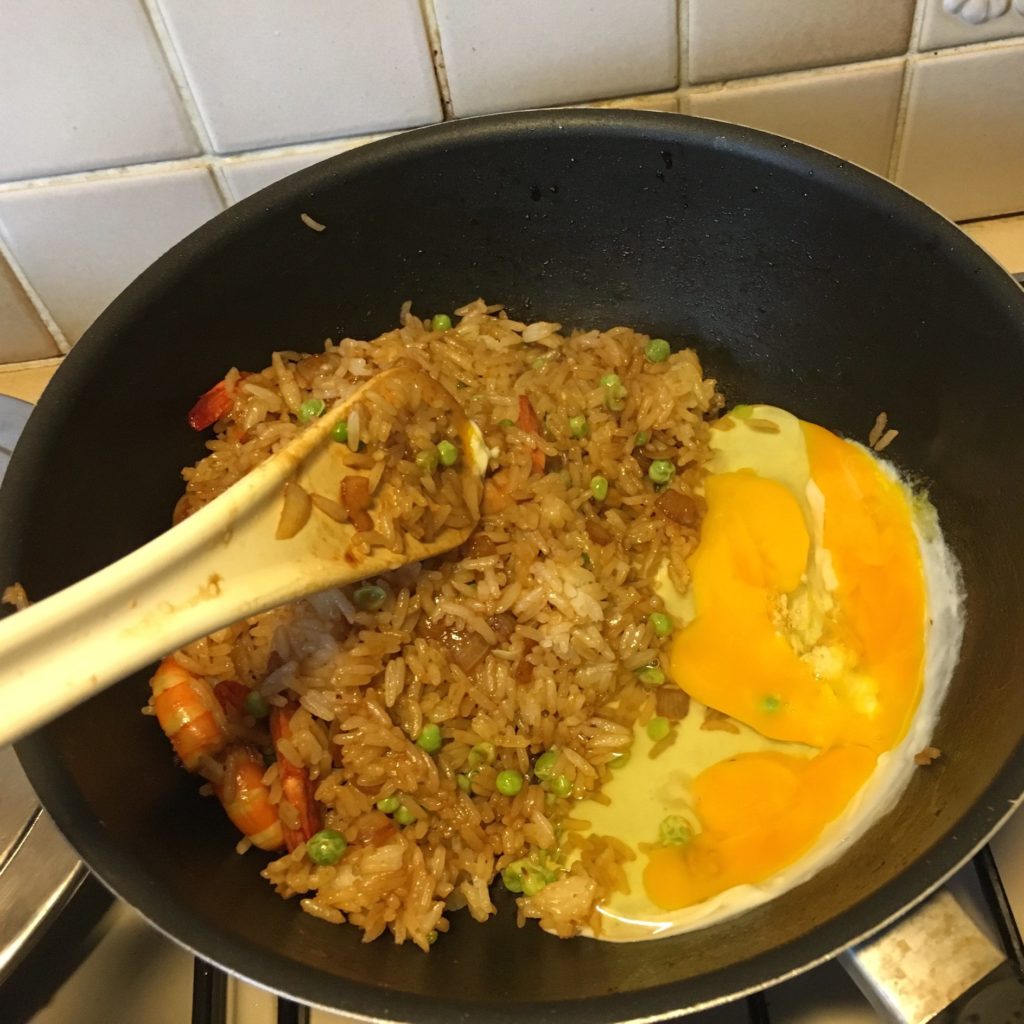 Sauteuse avec du riz, des crevettes et des petits pois en train de cuire. Des oeufs brouillés sur un côté de la sauteuse