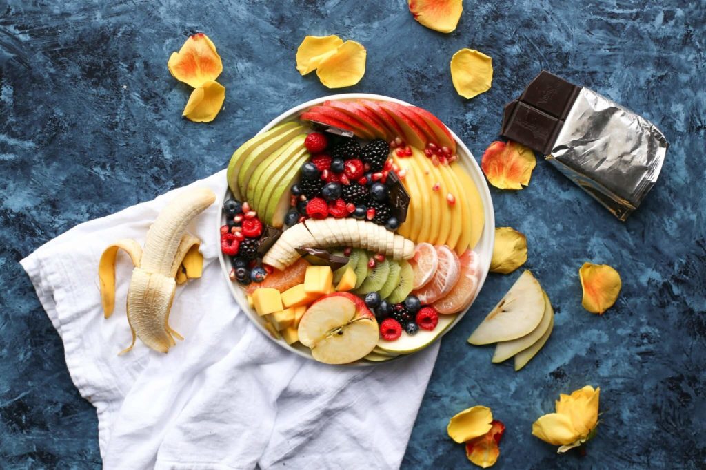 Bol de fruits tranchés posés sur une serviette blanche : banane, poires, fruits rouge, mangue et pommes