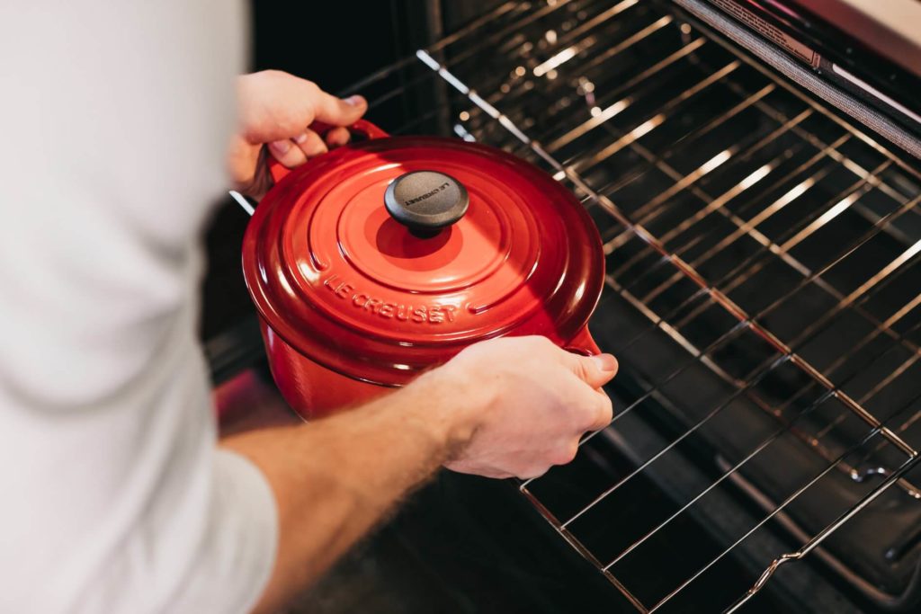 Mains d'un cuisinier qui sortent une cocotte rouge du four