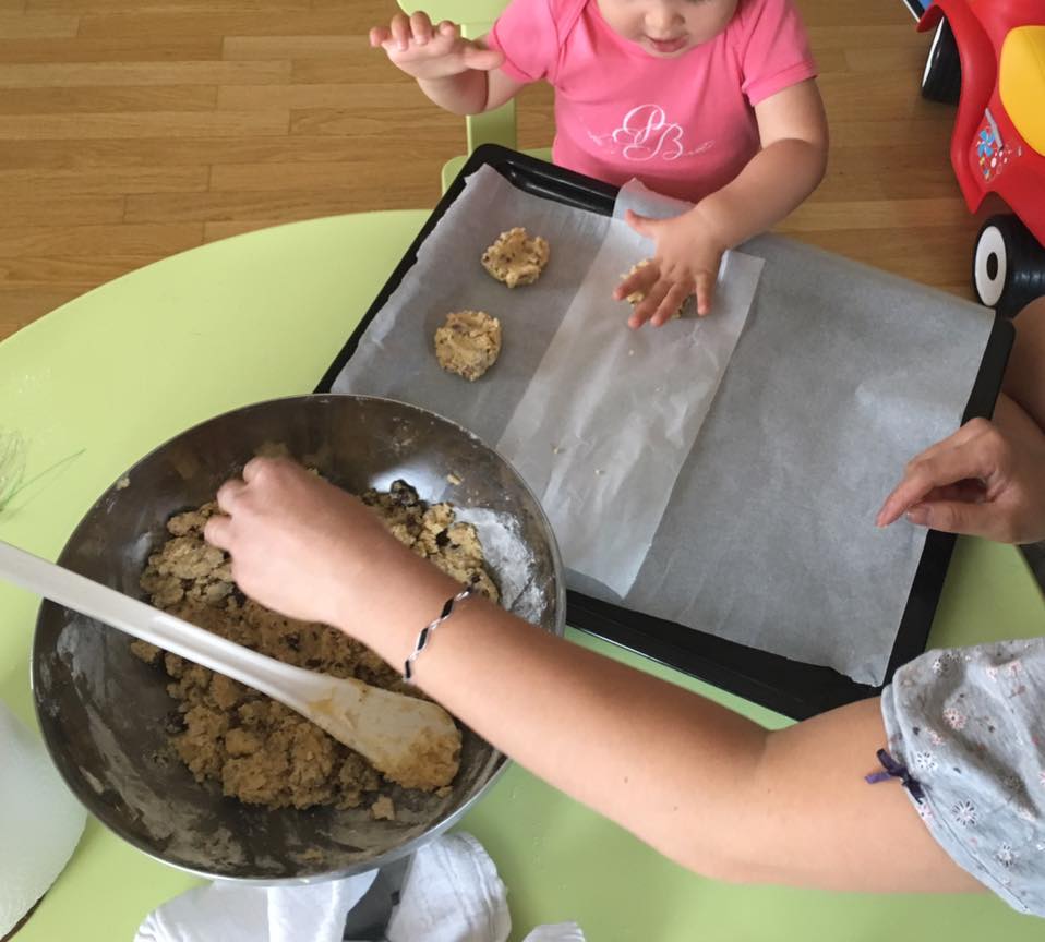 Main d'un enfant qui  aplati une pâte à biscuit sur une plaque de cuisson à côté des main d'une femme qui attrape un morceau de pâte dans un saladier