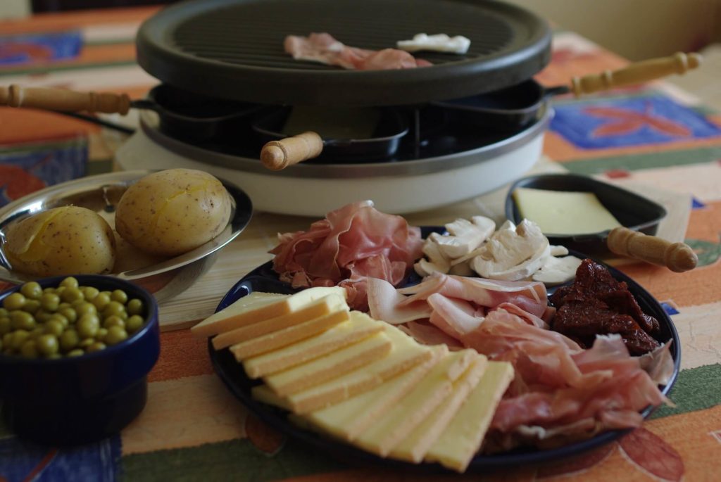 assiette de charcuterie et de formage à raclette devant un appareil à raclette