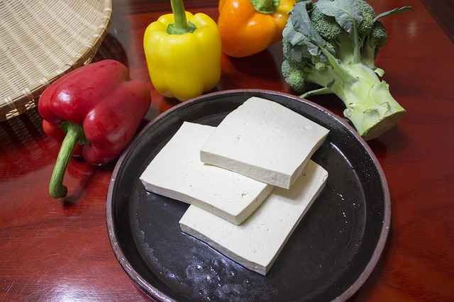 Tranches de tofu sur une assiette noire, entouré de poivrons rouge, jaune et orange et d'un brocoli entiers