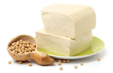 2 tranches de tofu fermes sur une assiette verte. A côté d'une cuillère en bois contenant des graines de soja.