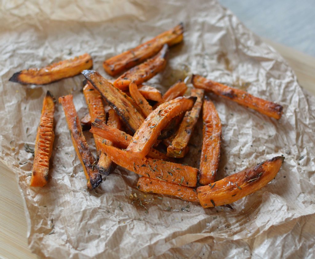 Frites oranges parsemées de thym et posées sur un papier marron