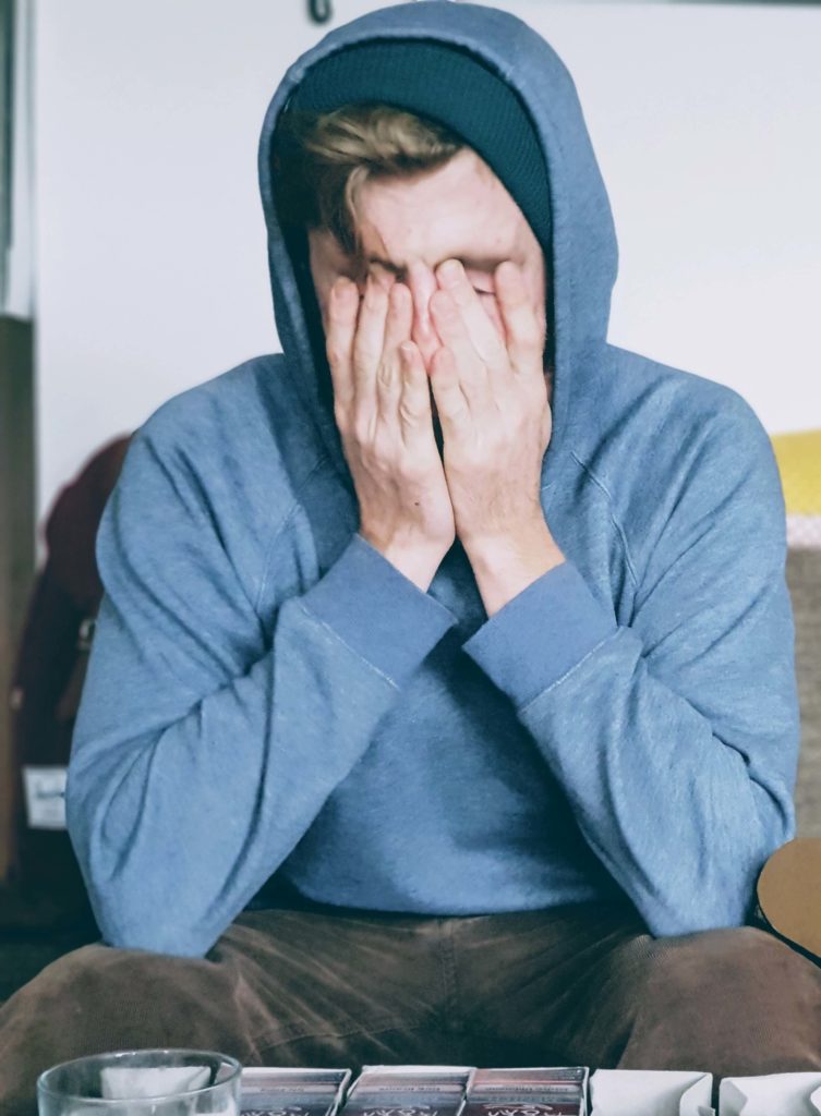 Homme assis portant un pull à capuche qui se frotte les yeux