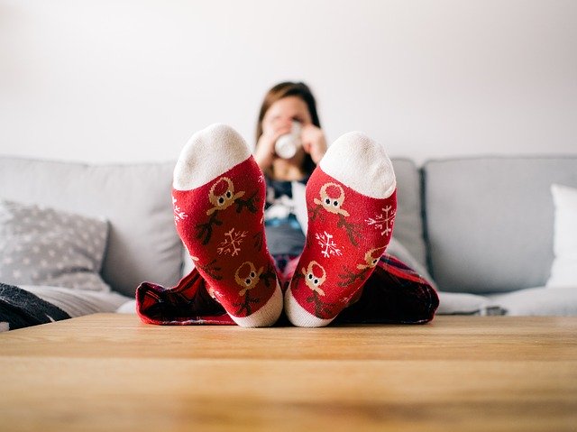 Femme assise dans un canapé avec des chaussettes rouges les pieds posés sur une table basse en train de boire dans une tasse