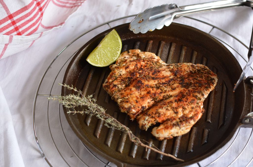 Filet de poulet sur un grill avec un morceau de citron vert et une branche de thym