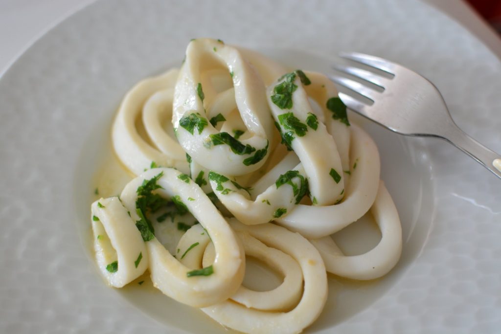 rondelles de calamars avec du persil haché dans une assiette blanche à côté d'une fourchette