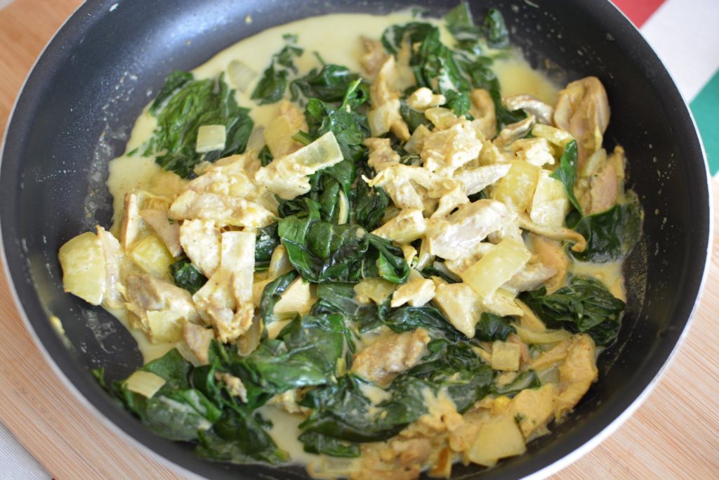 Morceaux de poulet dans une poêle avec des épinards dans une sauce jaune