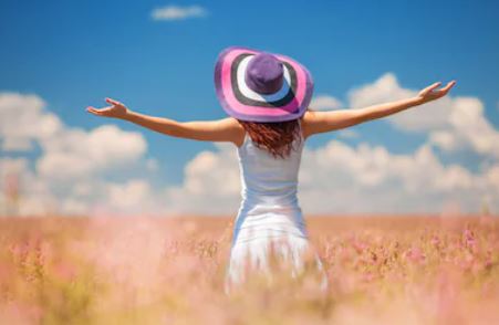 Femme debout de dos en robe blanche portant un chapeau dans un champ de blé,les bras écartés