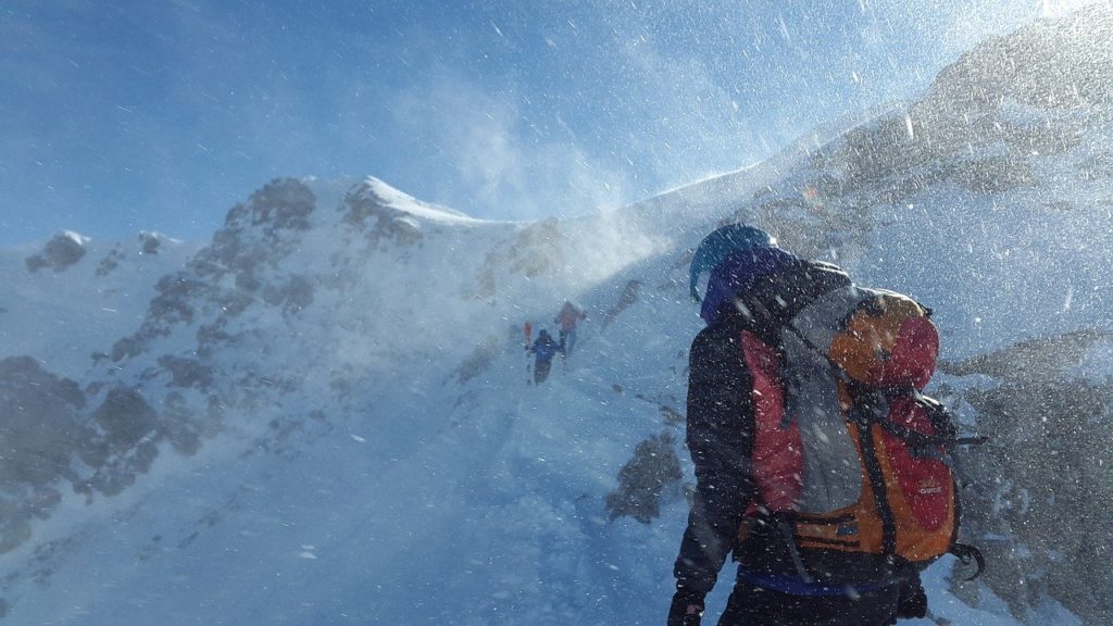 Personne de dos habillé avec un blouson et un sac à dos gravissant une montagne enneigée