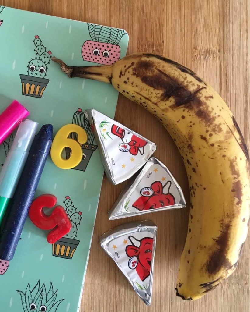 Banane posée avec des portions de fromage sur un cahier coloré et des crayons de couleurs