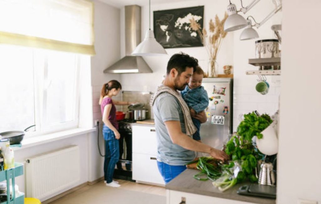 Une femme et un homme avec un bébé dans les bras qui cuisinent