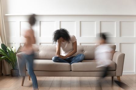 femme assise sur un canapé en se tenant la tête, avec des enfants qui courent