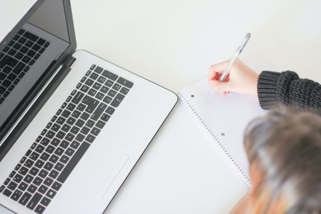 Femme qui écrit sur un cahier face à un ordinateur portable